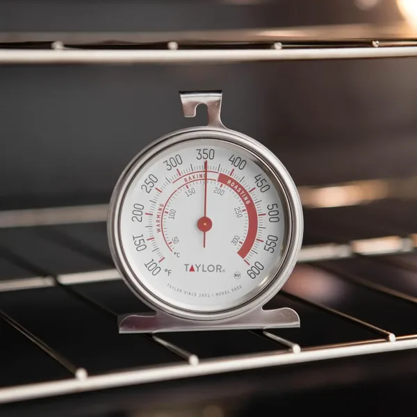 This Taylor stainless steel oven thermometer features a large, easy-to-read 3.25-inch dial with a red pointer, displaying temperatures from 100 to 600 degrees Fahrenheit, and is NSF certified for quality and durability, designed to either hang or stand inside your oven.